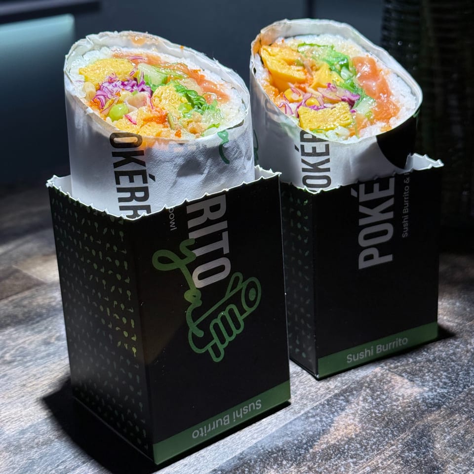Two colorful Pokérrito sushi burritos in branded black and green holders on a wooden surface.