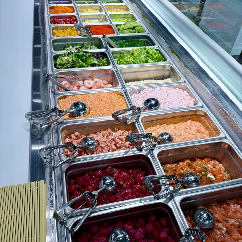 A vibrant poke bar with various fresh ingredients, including seafood, vegetables, and sauces, in metal containers.