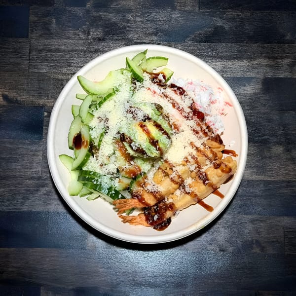 Pokérrito Ya poke bowl with fried shrimp, avocado, cucumber, and shredded cheese on dark wood.