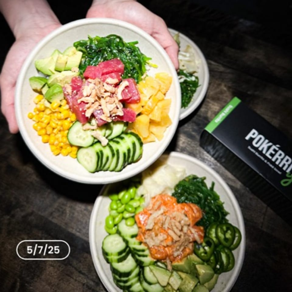 Two hands hold a poke bowl with tuna, avocado, corn, and pineapple, next to another bowl and a Pokérrito box.