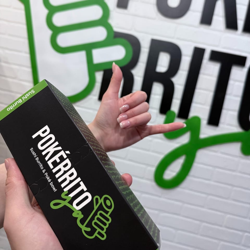 Hands holding a Pokérrito Ya sushi burrito box, with a shaka sign and restaurant logo in background.